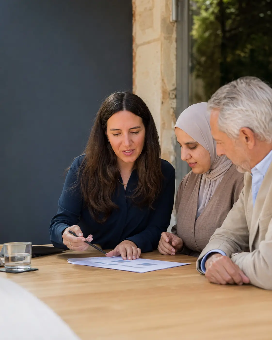 Zwei Beraterinnen von Therese Blau besprechen mit einem Kunden an einem Holztisch eine ausgedruckte Nachhaltigkeits-Roadmap.